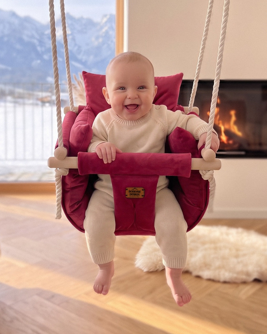 BOHOME Premium Babyschaukel Ruby Red – fröhliches Baby in der handgefertigten Schaukel im Wohnzimmer mit Alpenblick